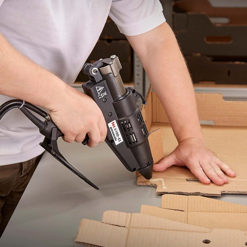 Worker forming a cardboard box using a hot glue gun
