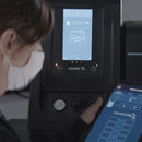 Operator using Meler Micron+ touchscreen control system with tablet interface for monitoring and adjusting adhesive settings.