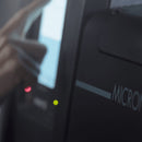 Close-up of Meler Micron+ hot melt adhesive melter housing with illuminated status indicators and touchscreen interface in the background.