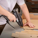 Hot melt adhesive is applied to corrugated cardboard using a pneumatic Power Adhesives Tec 6100 glue gun in a packaging workspace.