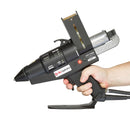 An operator holds the Tec 7100 hot melt glue gun from Power Adhesives, showing scale, handle ergonomics, and front nozzle orientation.